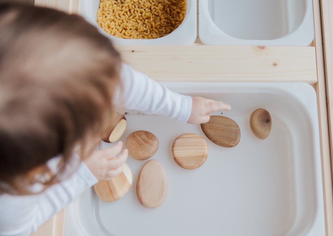 A toddler playing with wooden stones in a Montessori educational setup, promoting motor skills development.
