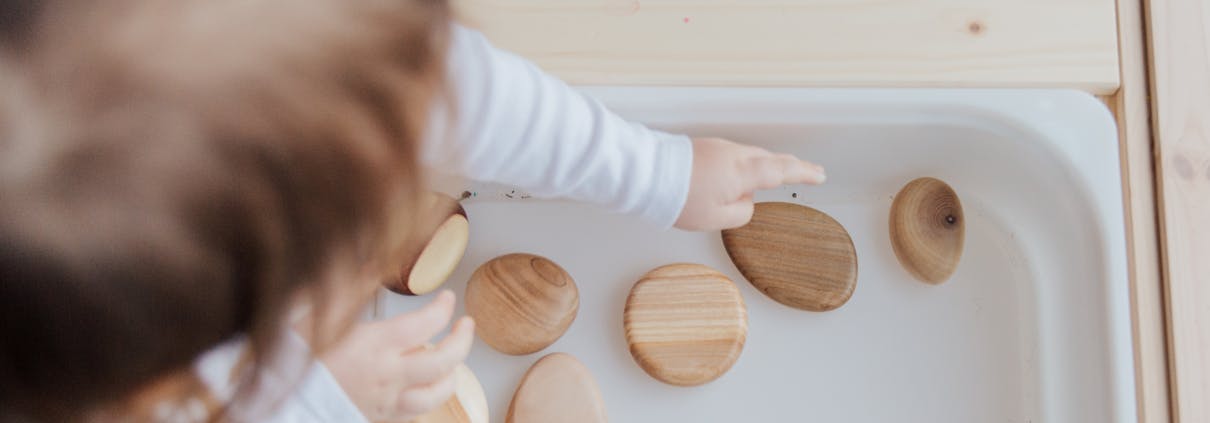 A toddler playing with wooden stones in a Montessori educational setup, promoting motor skills development.