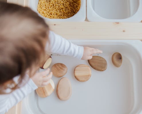 A toddler playing with wooden stones in a Montessori educational setup, promoting motor skills development.