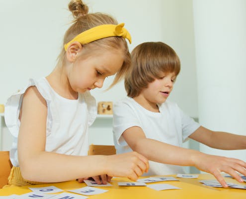 Two young children engaged in a fun learning activity indoors, focusing on letters.