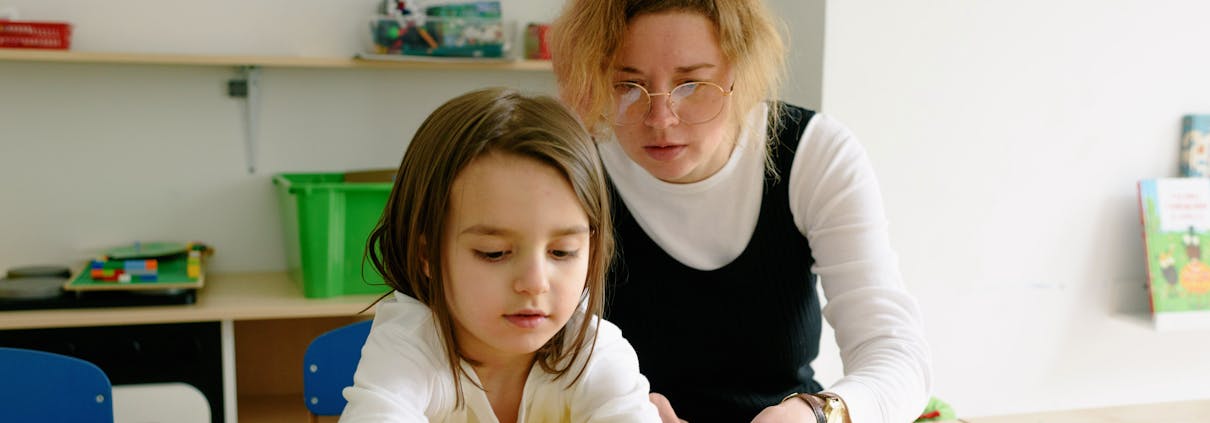 A child and teacher work together on an educational activity in a classroom setting.