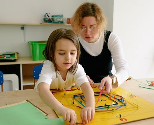 A child and teacher work together on an educational activity in a classroom setting.