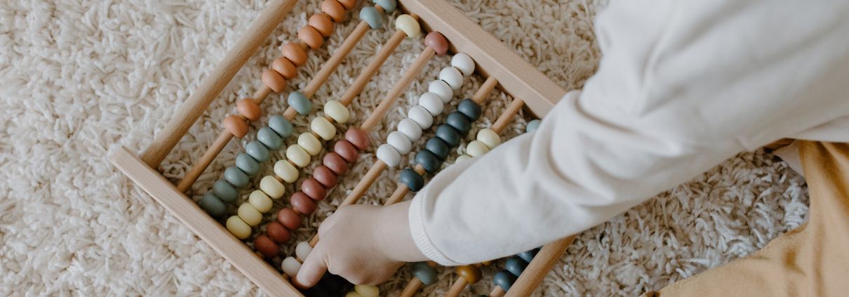 A young child interacts with a colorful wooden abacus, exploring learning through play.