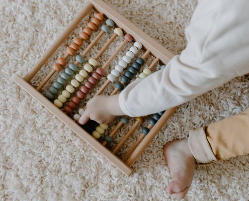 A young child interacts with a colorful wooden abacus, exploring learning through play.